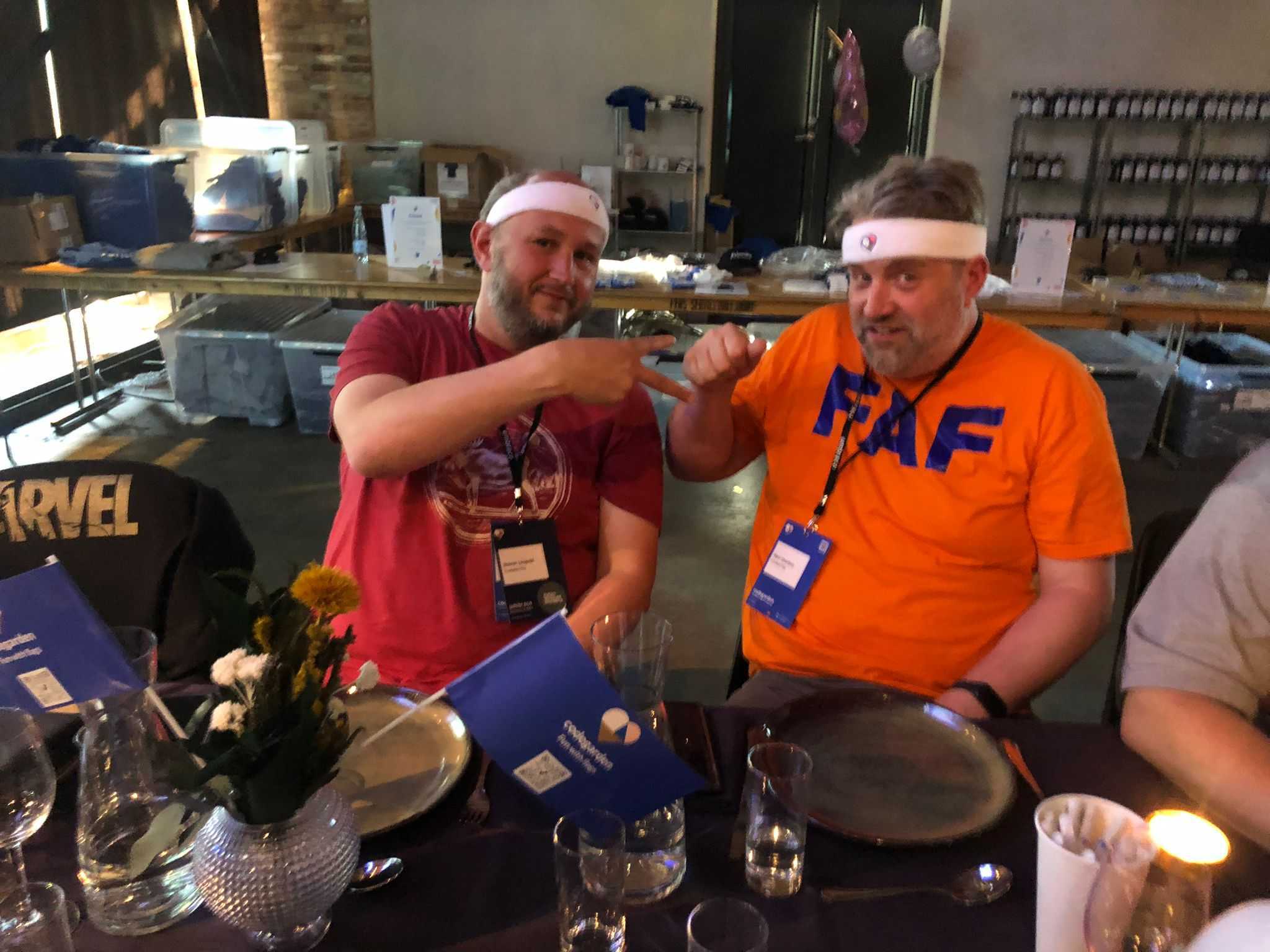 Image of two team members from Crumpled Dog, both wearing sports-style sweatbands. One of them is making the shape of scissors with his hands, and the other is making a rock shape, for a game of rock, paper, scissors.