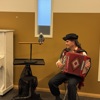 An African grey parrot on a perch with a man playing the Accordion