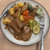A mixture of potatoes, broccoli, grilled onions, picked cucumbers and veal with gravy.