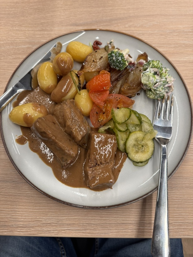 A mixture of potatoes, broccoli, grilled onions, picked cucumbers and veal with gravy.