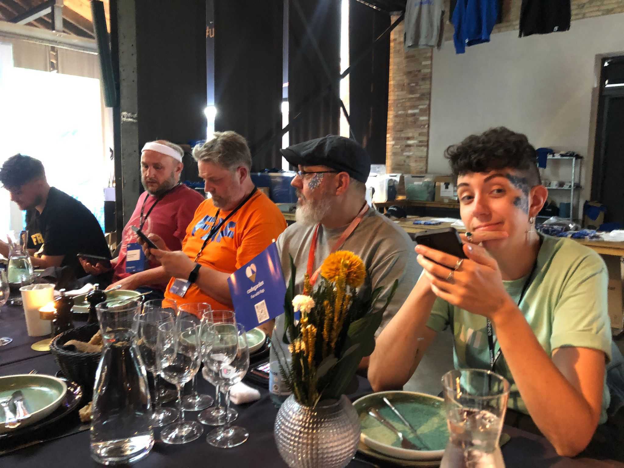 A picture of four team members from Crumpled Dog sitting at a dinner table. Two of them have face-painted designs, and one of them is wearing a sports-style sweatband.