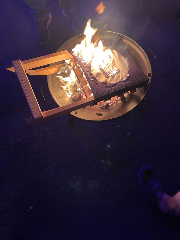 A wooden beach chair burning in a fire pit